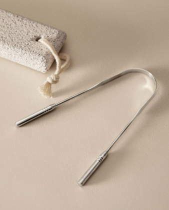 Stainless steel tongue scraper resting beside a washcloth